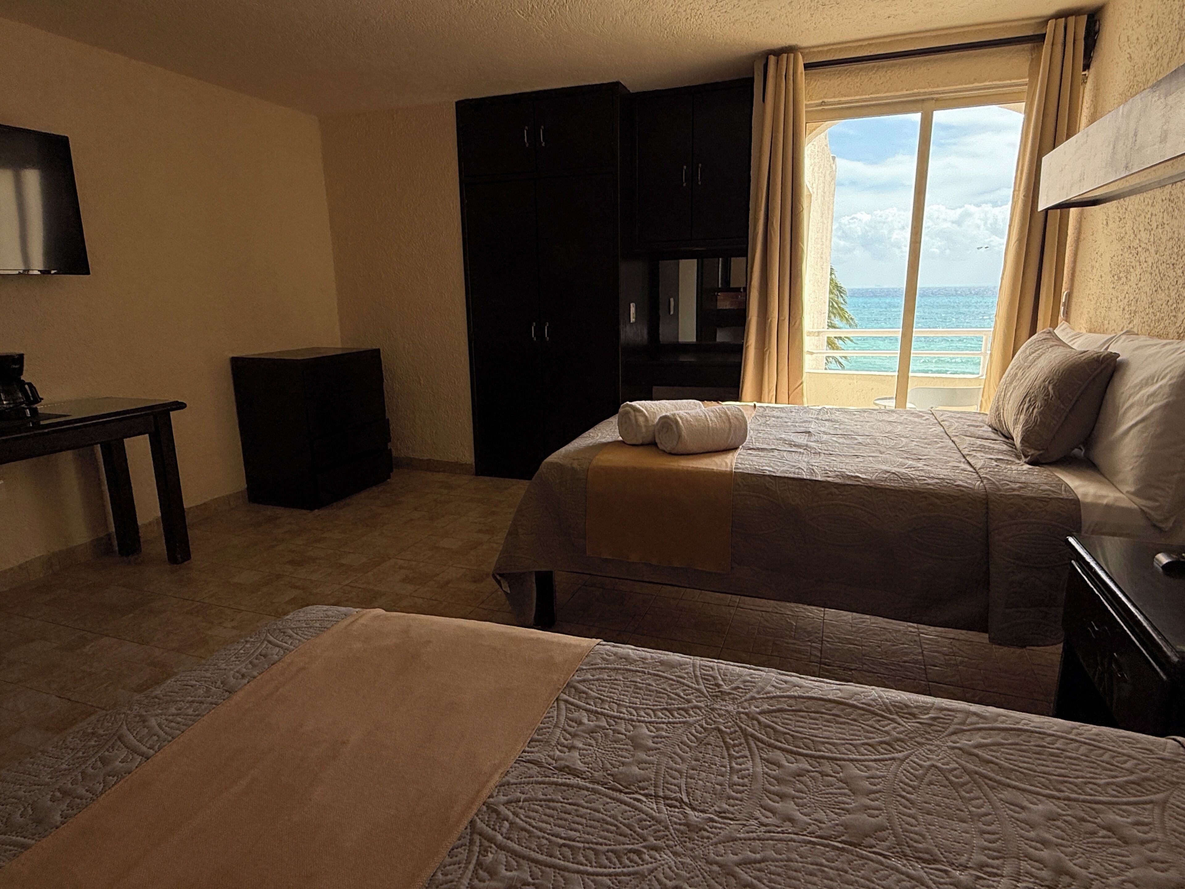 A hotel room with a bed, a desk, a wardrobe, and a view of the sea.