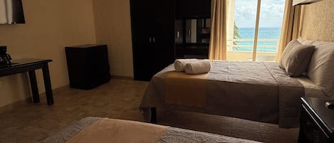 A hotel room with a bed, a desk, a wardrobe, and a view of the sea.