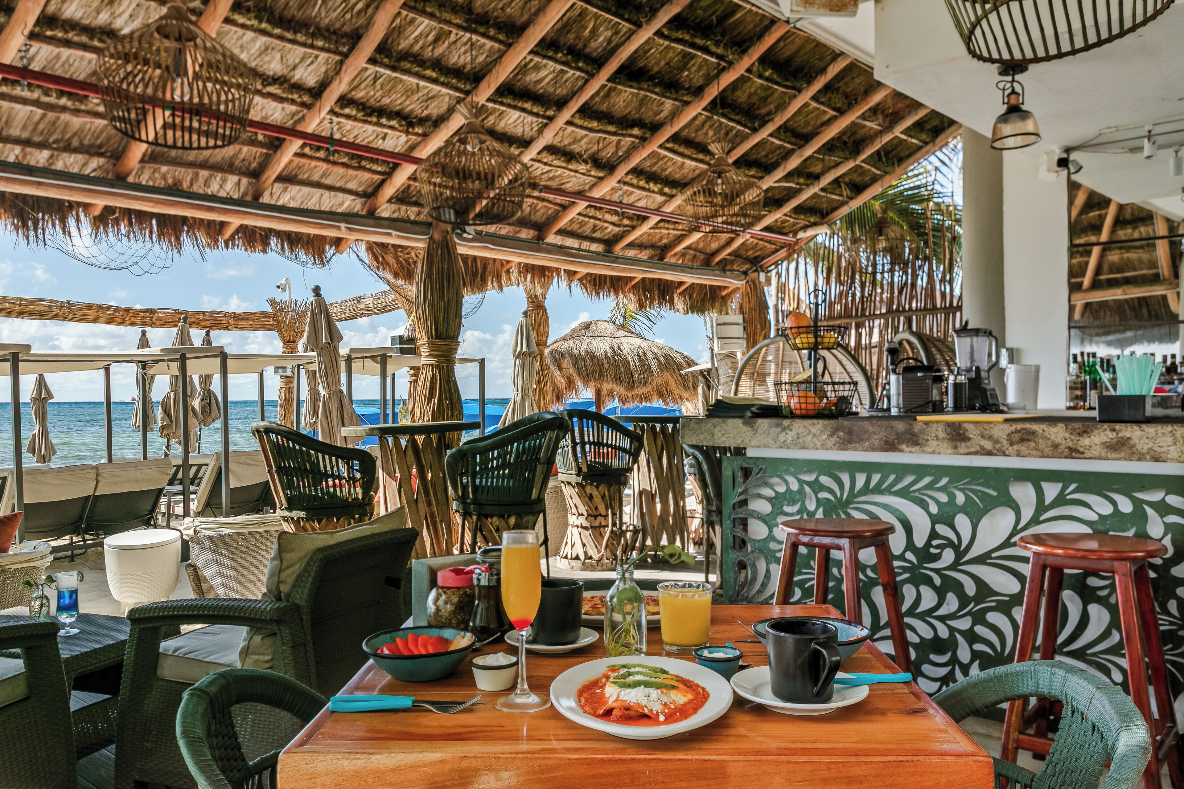 Un restaurante con techo de paja, mesas al aire libre y vistas al mar.