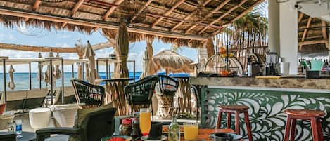Un restaurante con techo de paja, mesas al aire libre y vistas al mar.
