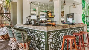 Una zona de bar con pared decorada, taburetes y una barra con diversos objetos.