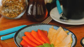 A wooden table with a bowl of sliced vegetables, a jar of nuts, a pepper grinder, and a plate of food.