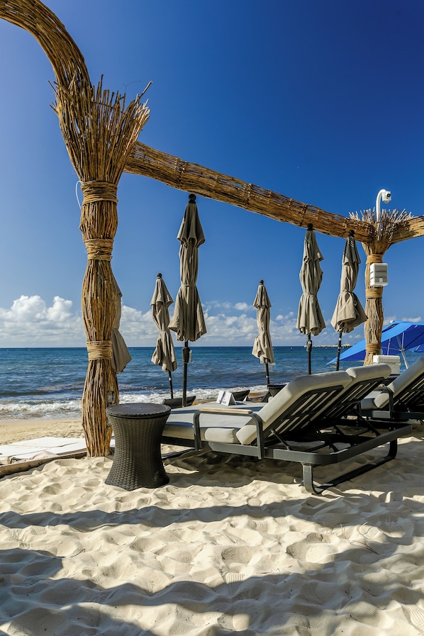 Ein Strand mit Liegestühlen, Sonnenschirmen und einer strohgedeckten Struktur.