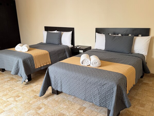 A hotel room with two beds, each with a grey quilted bedspread and a brown blanket. There are two white towels on each bed.