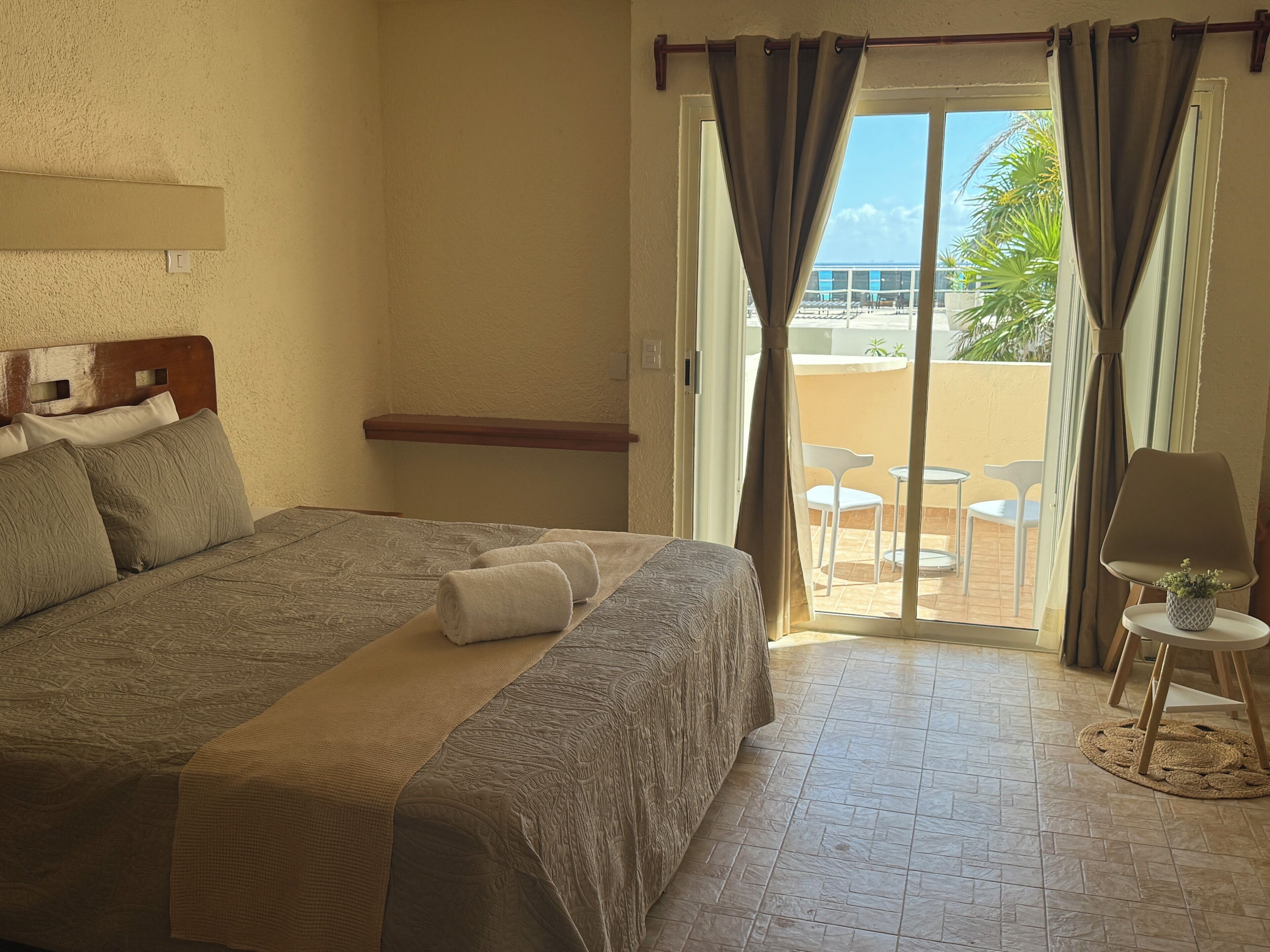 Ein Hotelzimmer mit einem Bett, einem kleinen Tisch mit Lampe und Blick auf den Außenbereich durch eine Schiebetür.