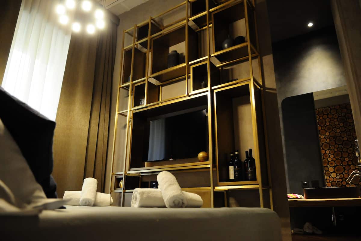 A hotel room with a large bed, a TV, and a built-in shelf with bottles.