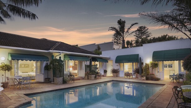 Uma área à beira da piscina com espreguiçadeiras, piscina e uma casa com várias portas e janelas.