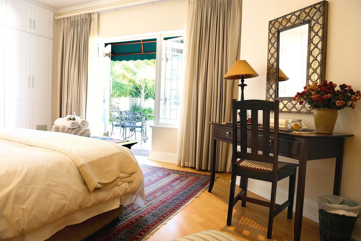 A bedroom with a bed, a desk, a chair, a lamp, a mirror, and a window with curtains.