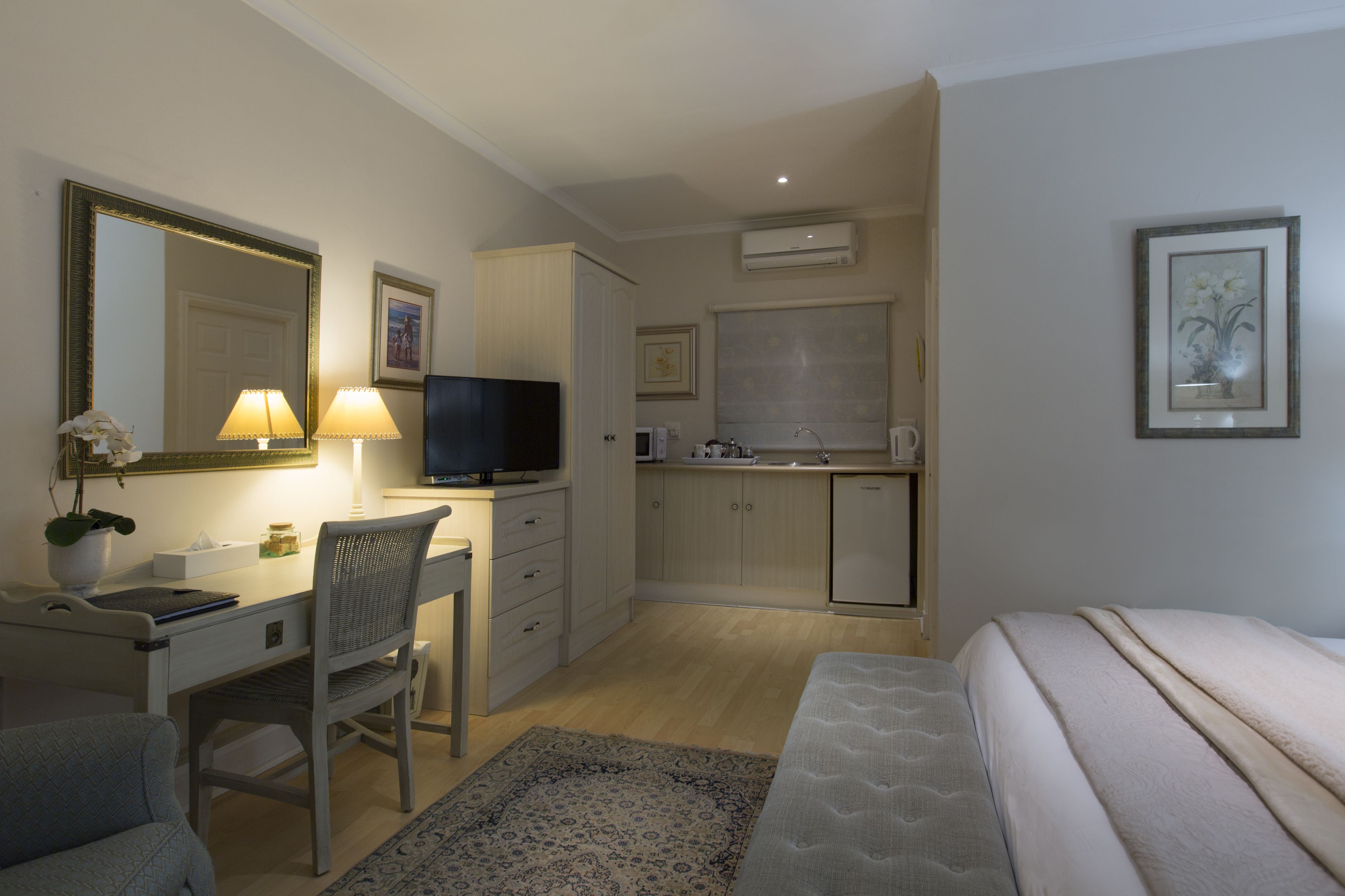 Quarto de hotel compacto com cama, escrivaninha com cadeira, televisão, pequena cozinha e banheiro.