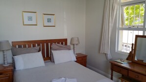 Een slaapkamer met een houten hoofdeinde, een bed met wit en beige beddengoed, twee nachtkastjes met lampen, een dressoir en een raam met gordijnen.