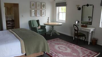 A bedroom with a bed, a green armchair, a desk with a chair, a round table, and a large mirror.