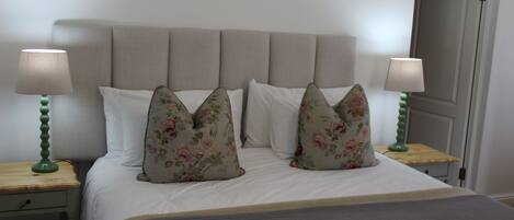 Cama bem arrumada com almofadas florais, duas luminárias de mesa e uma mesinha de cabeceira de madeira.