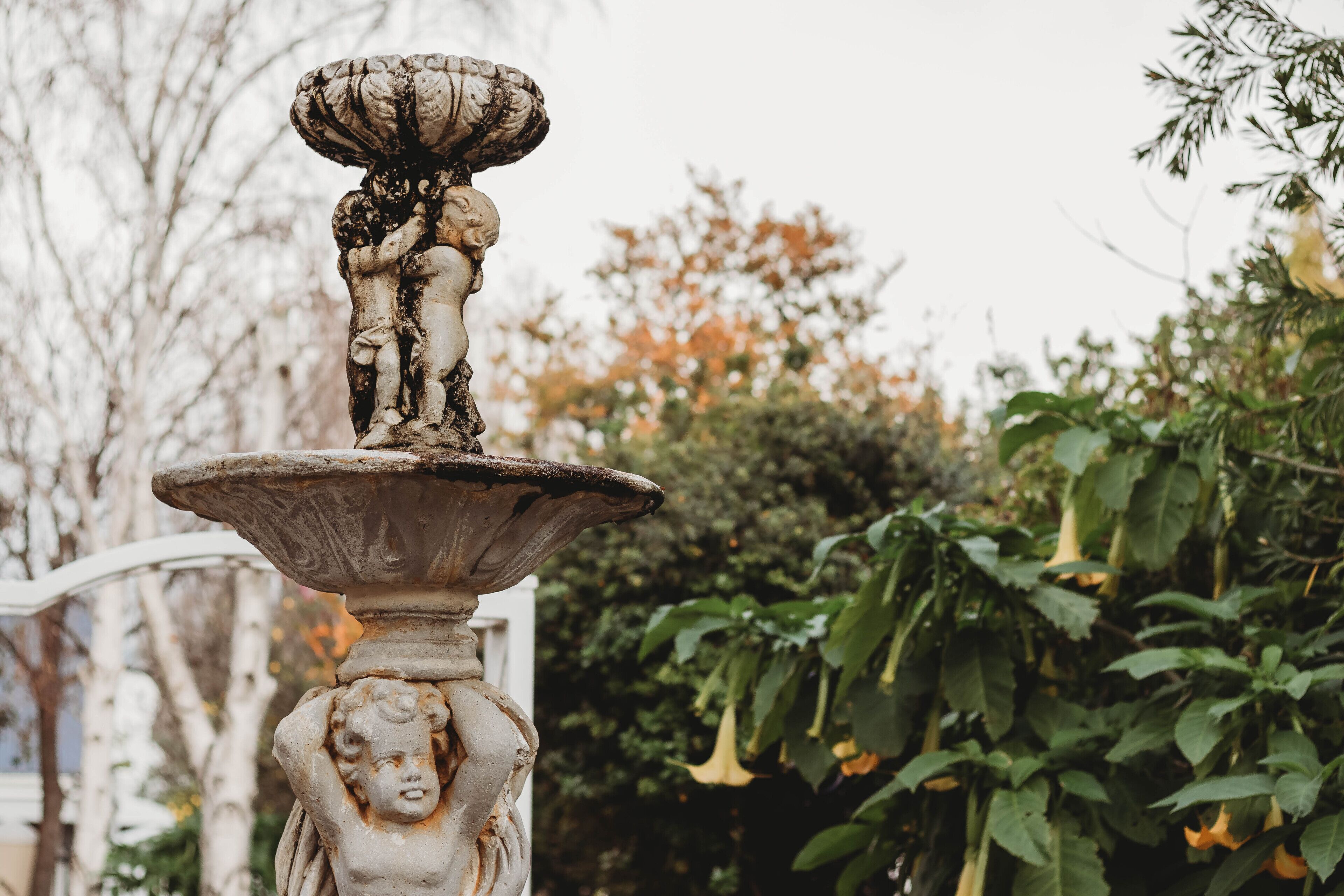 A stone fountain with a statue of a figure holding a child, surrounded by greenery.
