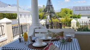 A checkered table set outdoors with a white column, a metal structure, and a building in the background. - Le Petit Paris (Franschhoek)
