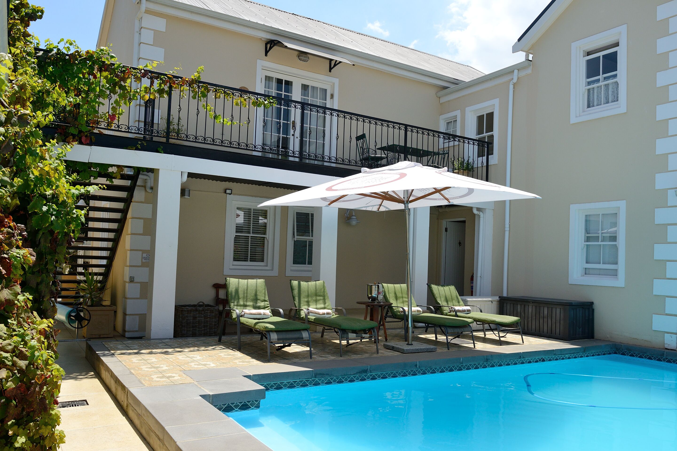 A swimming pool with lounge chairs and an umbrella, a staircase, and a balcony with a railing.