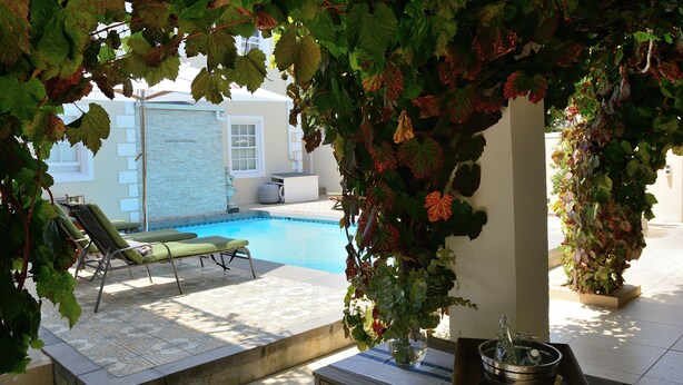 A poolside area with a lounge chair, a table with a bowl and a bottle, and a potted plant. - Le Petit Paris (Franschhoek)