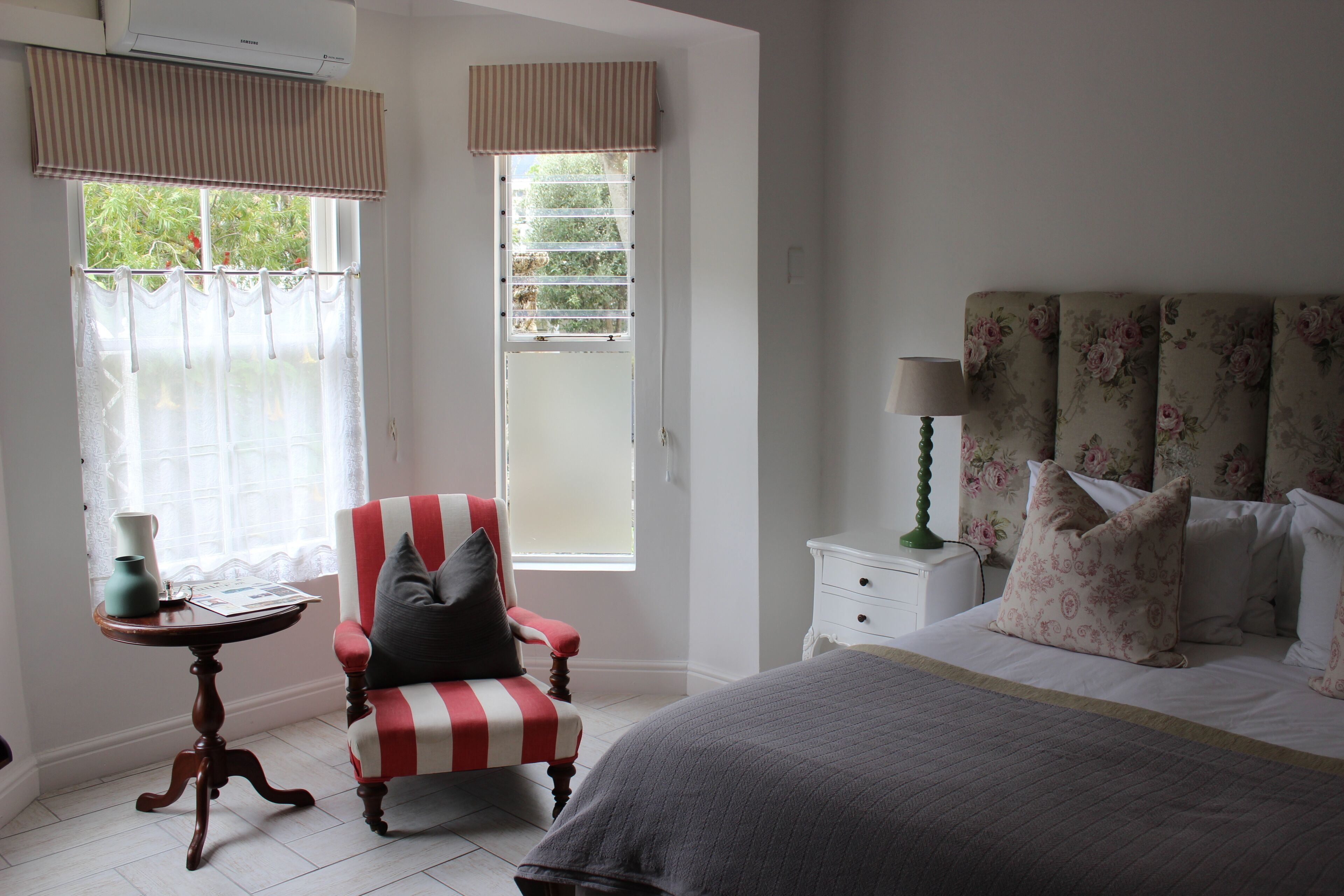 A bedroom with a bed, a chair, a nightstand, a lamp, and a window with curtains.
