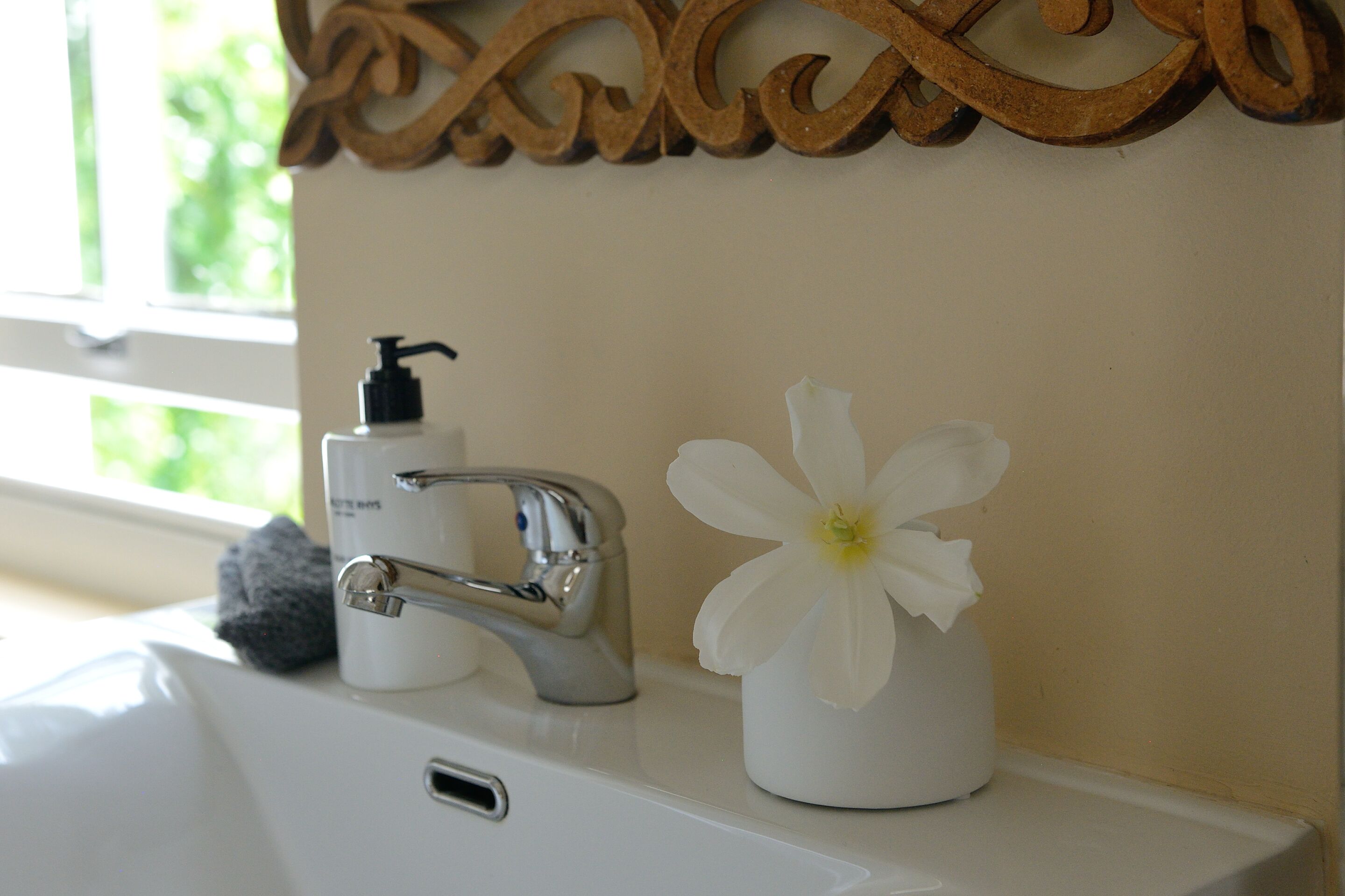 A bathroom sink with a faucet, a soap dispenser, and a flower in a vase.