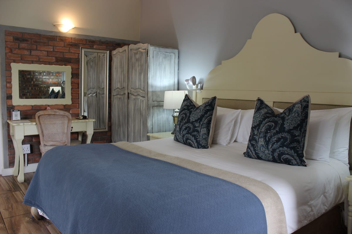 A bedroom with a large bed, a desk, a chair, and a wardrobe.