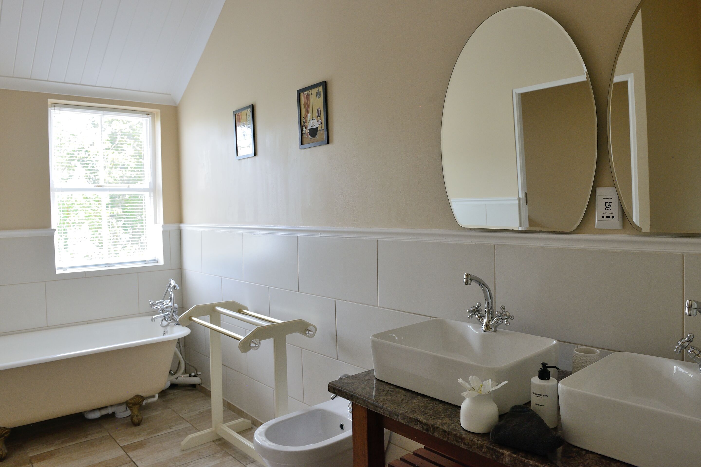 A bathroom with a bathtub, two sinks, a toilet, and a window.