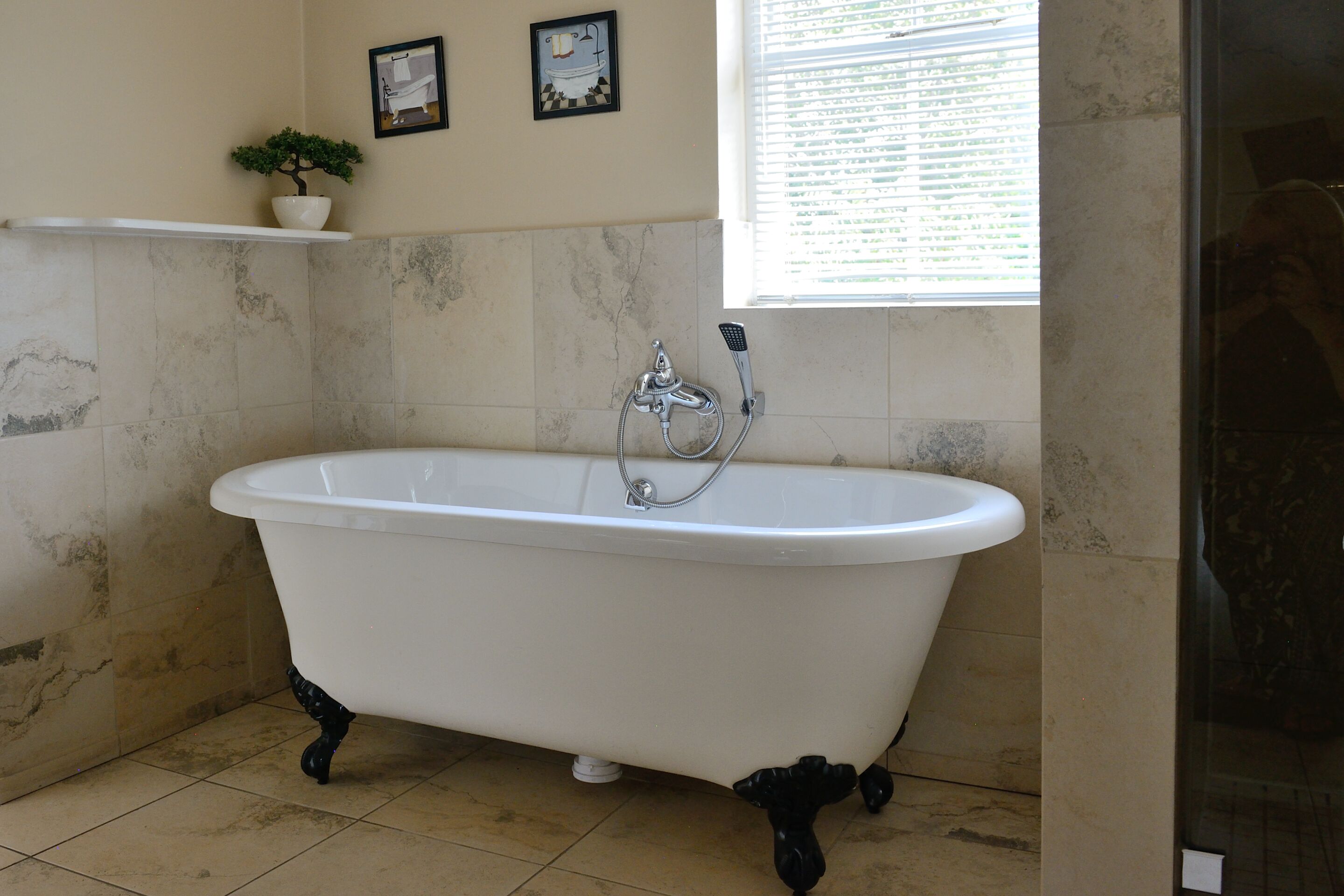 A clawfoot bathtub in a bathroom with tiled walls and a window.