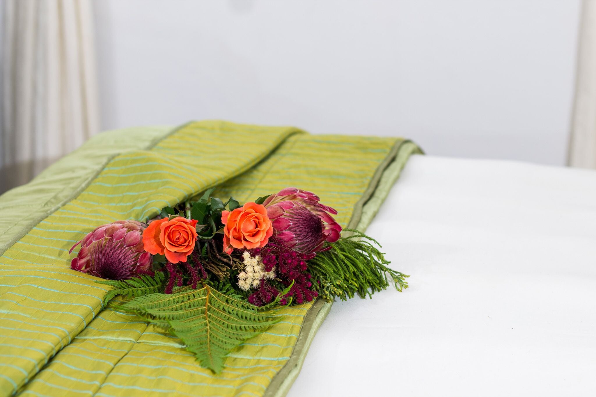 Un lit recouvert d’une couette verte et agrémenté d’un arrangement floral.