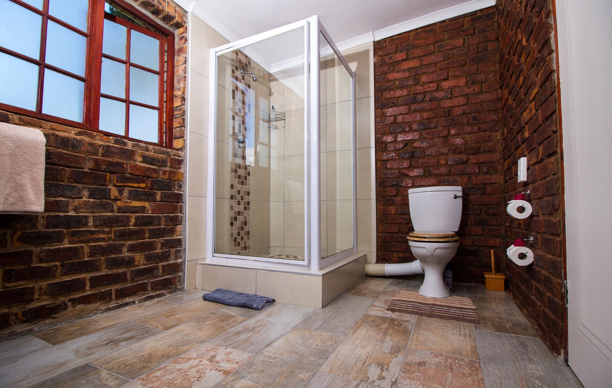 Un baño con ducha, inodoro y pared de ladrillo.