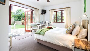 Un dormitorio con cama, escritorio y silla. Hay una ventana con cortinas y vistas al jardín.