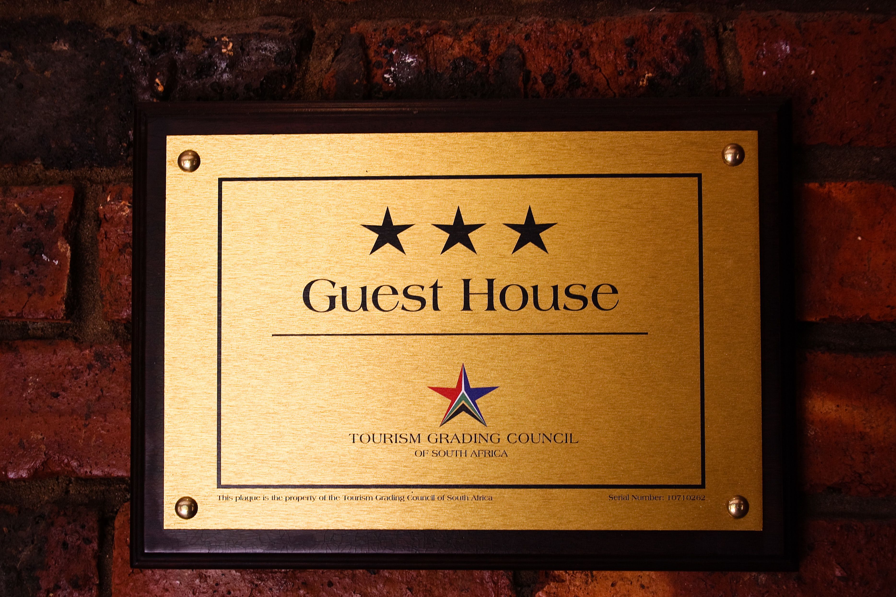Une plaque fixée à un mur de briques, portant l’inscription « Maison d’hôtes » et le logo du Conseil sud-africain de classification des établissements touristiques.