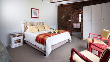A bedroom with a bed, a nightstand, a chair, a wardrobe, and a brick wall.