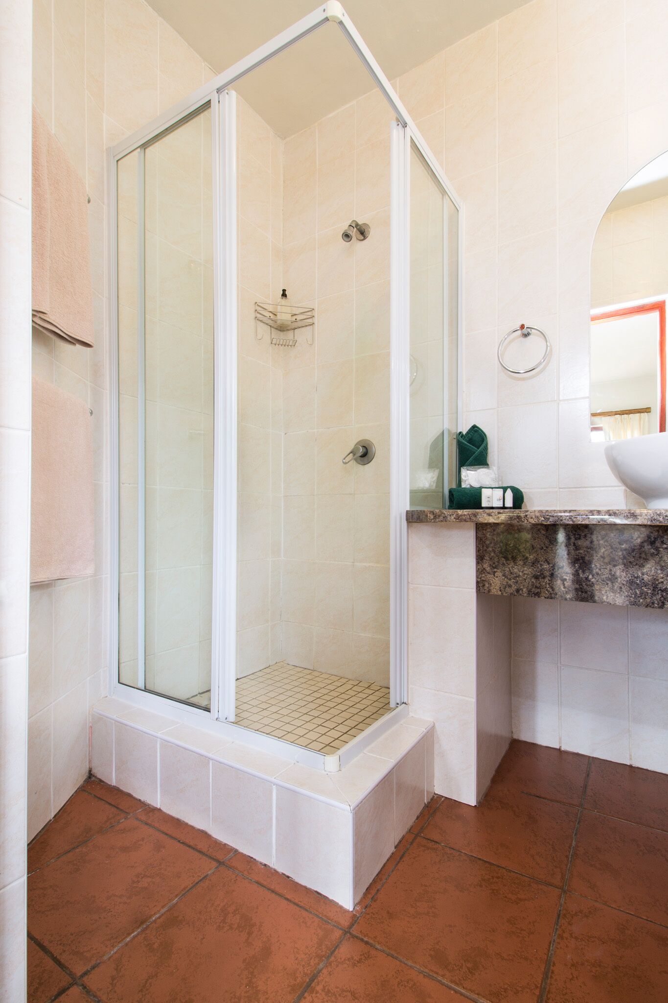 A bathroom with a glass-enclosed shower, white tiled walls, a sink with a granite countertop, and a mirror.