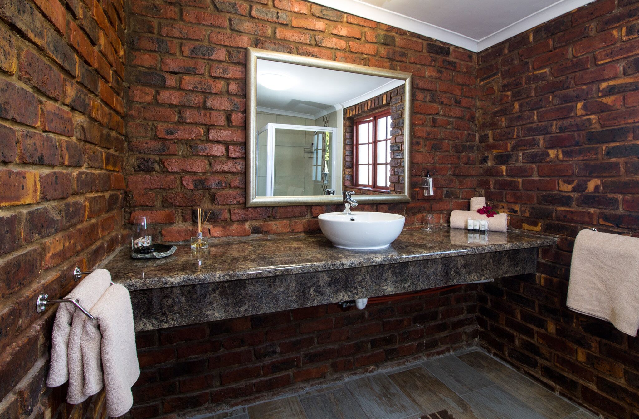 A bathroom with a brick wall, a large mirror, a white sink, and a towel rack.