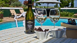 Une table au bord de la piscine avec une bouteille de vin, deux verres et des amuse-gueules.