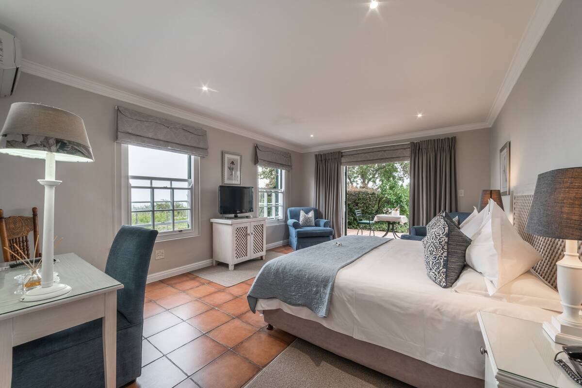 Un dormitorio con cama, escritorio, silla, televisor y vista al exterior.