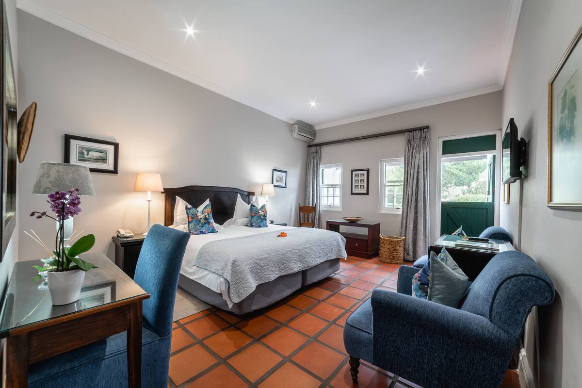 Una habitación de hotel con cama, escritorio, silla, televisor y ventana con cortinas.