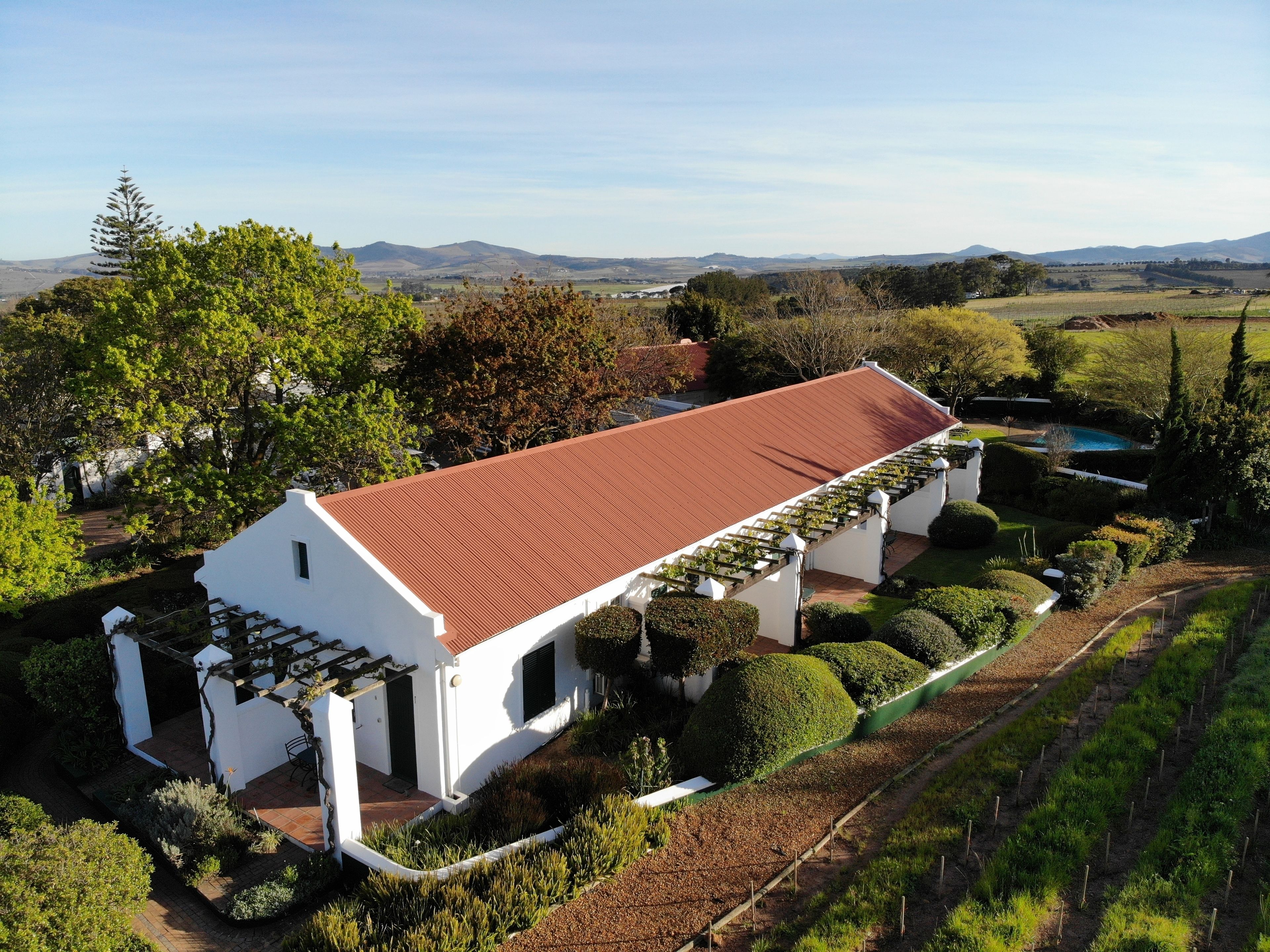 A white building with a red roof, surrounded by well-maintained gardens and a pool.