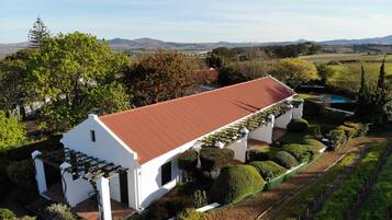 A white building with a red roof, surrounded by well-maintained gardens and a pool.