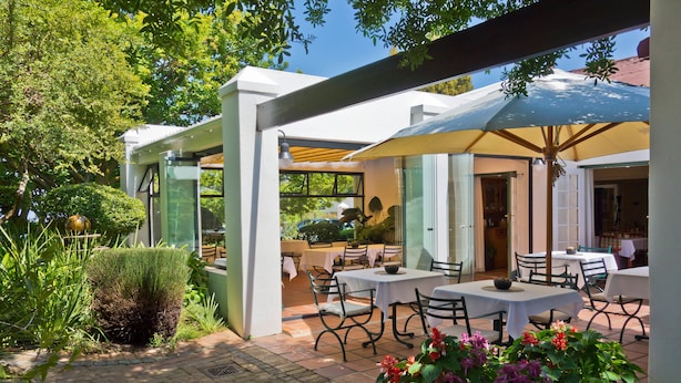 Un espace extérieur aménagé en terrasse, avec des tables et des chaises, entouré de verdure et doté d  ’une pergola offrant de l’ombre.
