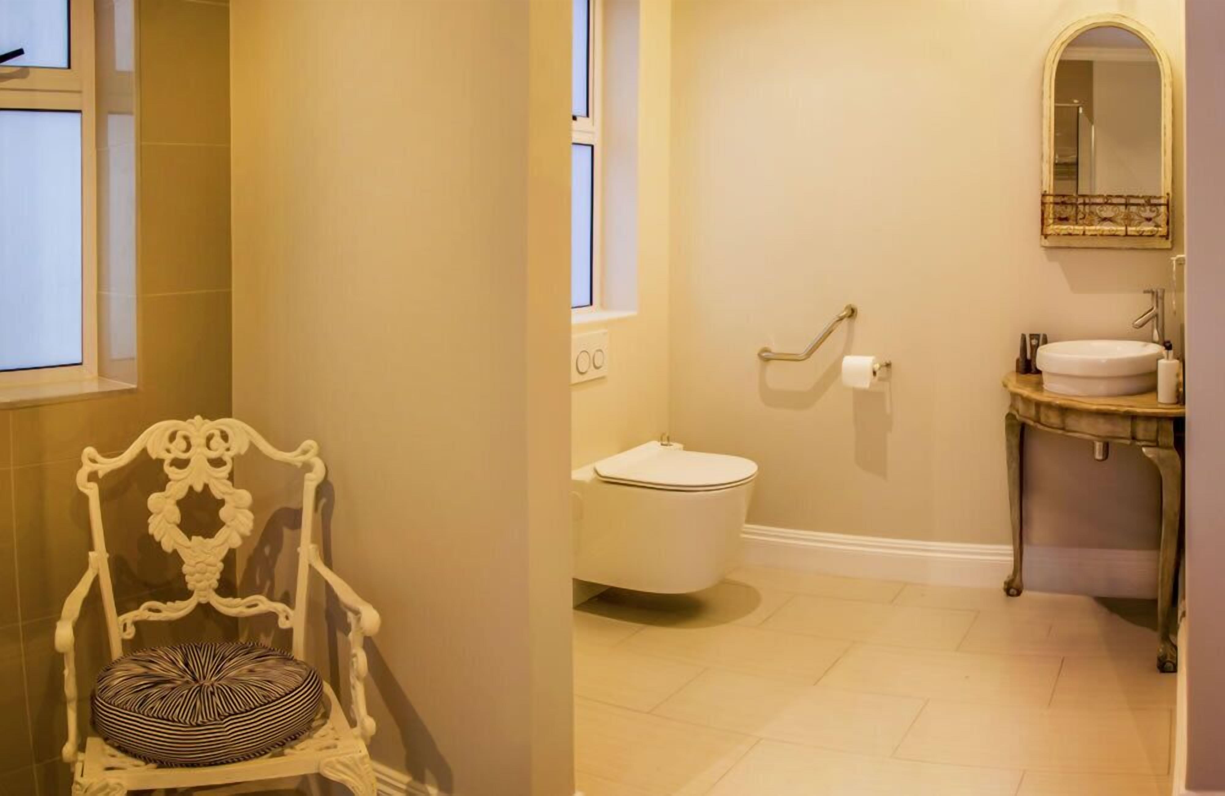 Ein Badezimmer mit Toilette, Waschbecken, Spiegel und einem Sessel mit gemustertem Kissen.