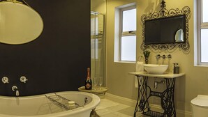 A bathroom with a freestanding bathtub, a vintage sewing machine vanity, a large mirror, and a window.