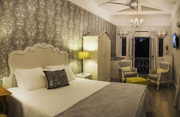 A bedroom with a large bed, a nightstand, a lamp, two armchairs, a small table, and a ceiling fan.
