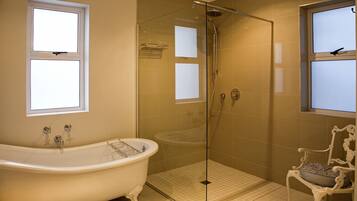A bathroom with a freestanding bathtub, a glass-enclosed shower, and a white chair with a striped cushion.