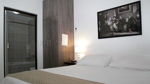 A hotel room with a bed, a wooden wardrobe, a framed picture on the wall, and a bathroom with a glass door. - Broadway Tygervalley (Cape Town)