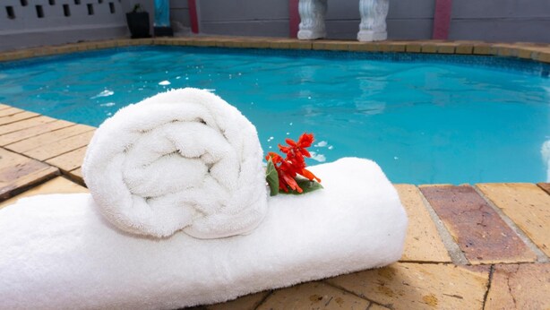 A poolside area with a white towel and a small bouquet of red flowers. - Broadway Tygervalley (Cape Town)