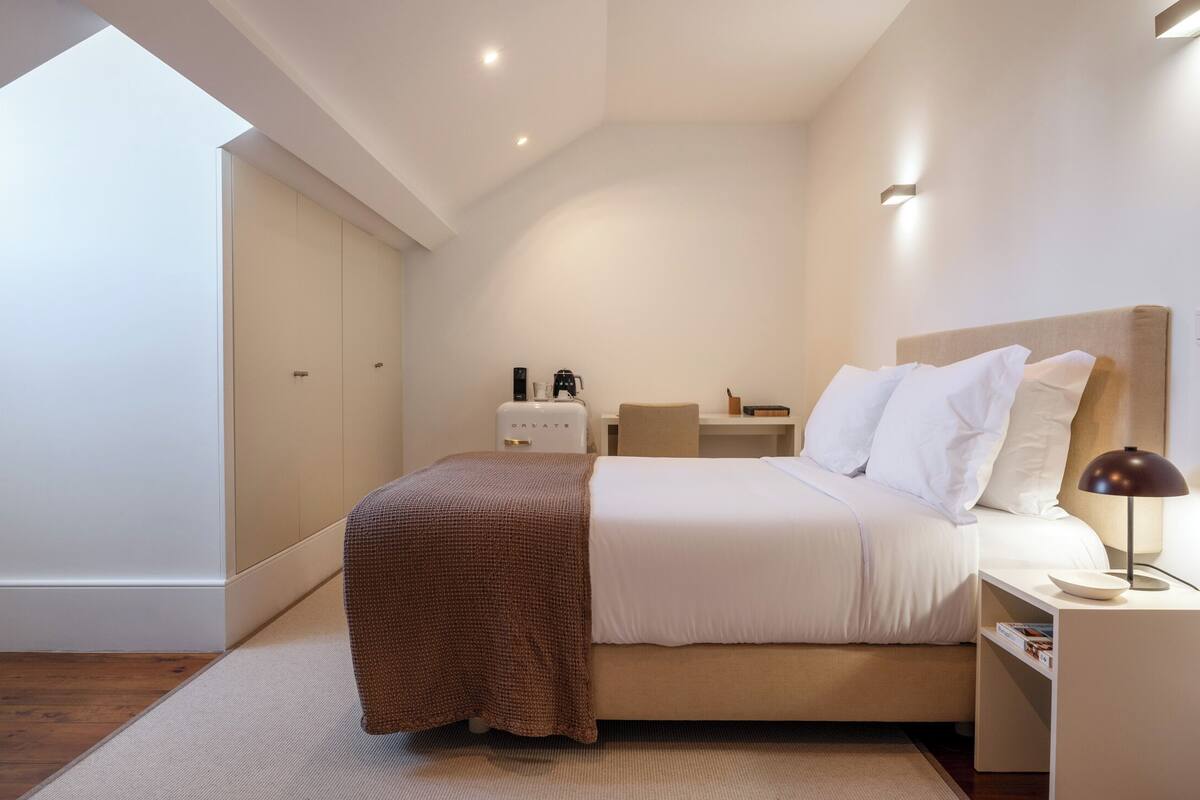 A modern bedroom with a bed, bedside table, lamp, and a coffee machine.