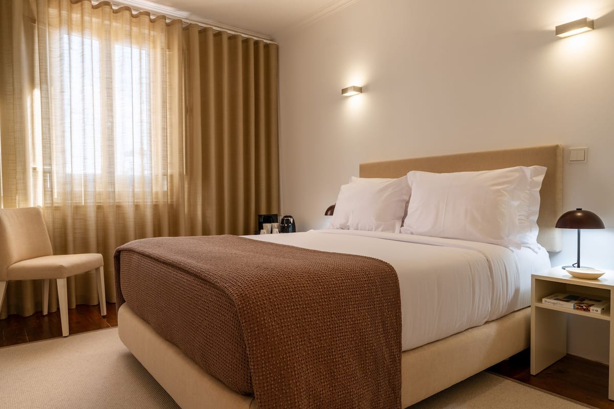A hotel room with a bed, a chair, a nightstand, and a lamp.