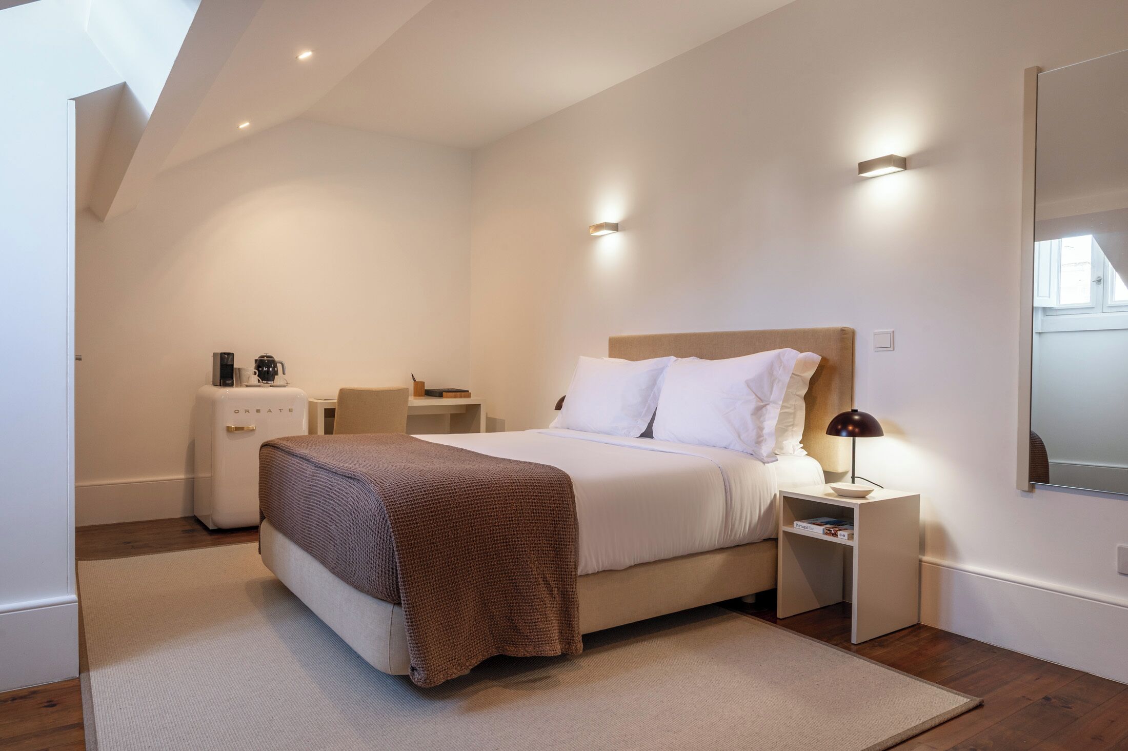 A modern bedroom with a bed, bedside tables, a nightstand, a coffee machine, and a mirror.