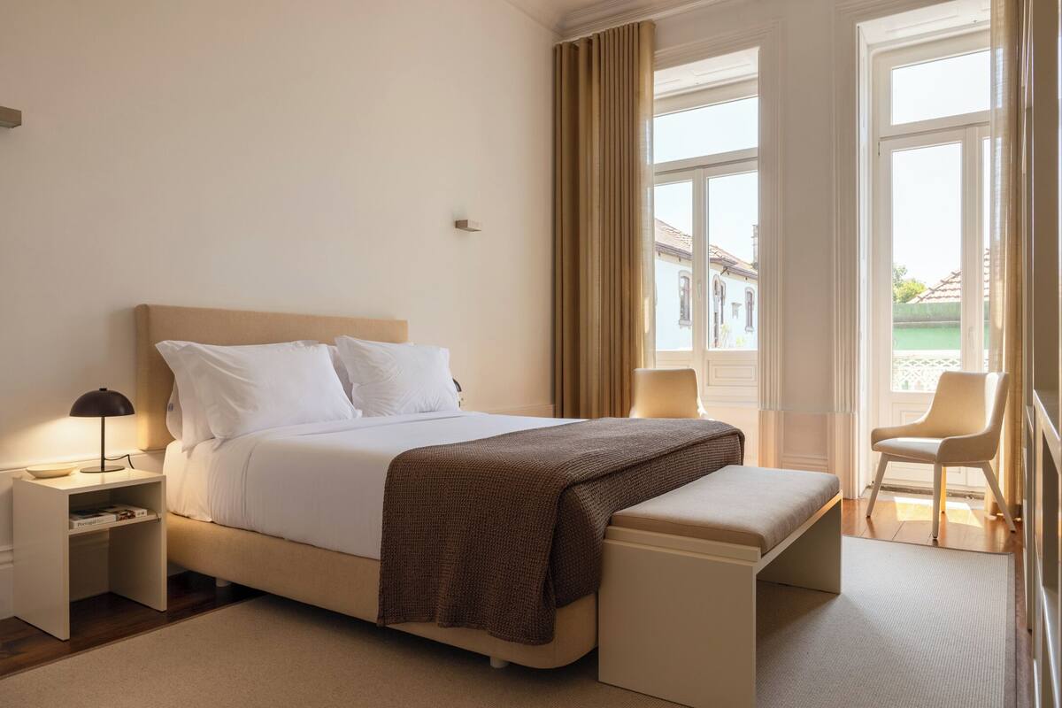 A hotel room with a bed, bedside tables, a bench, and a chair.