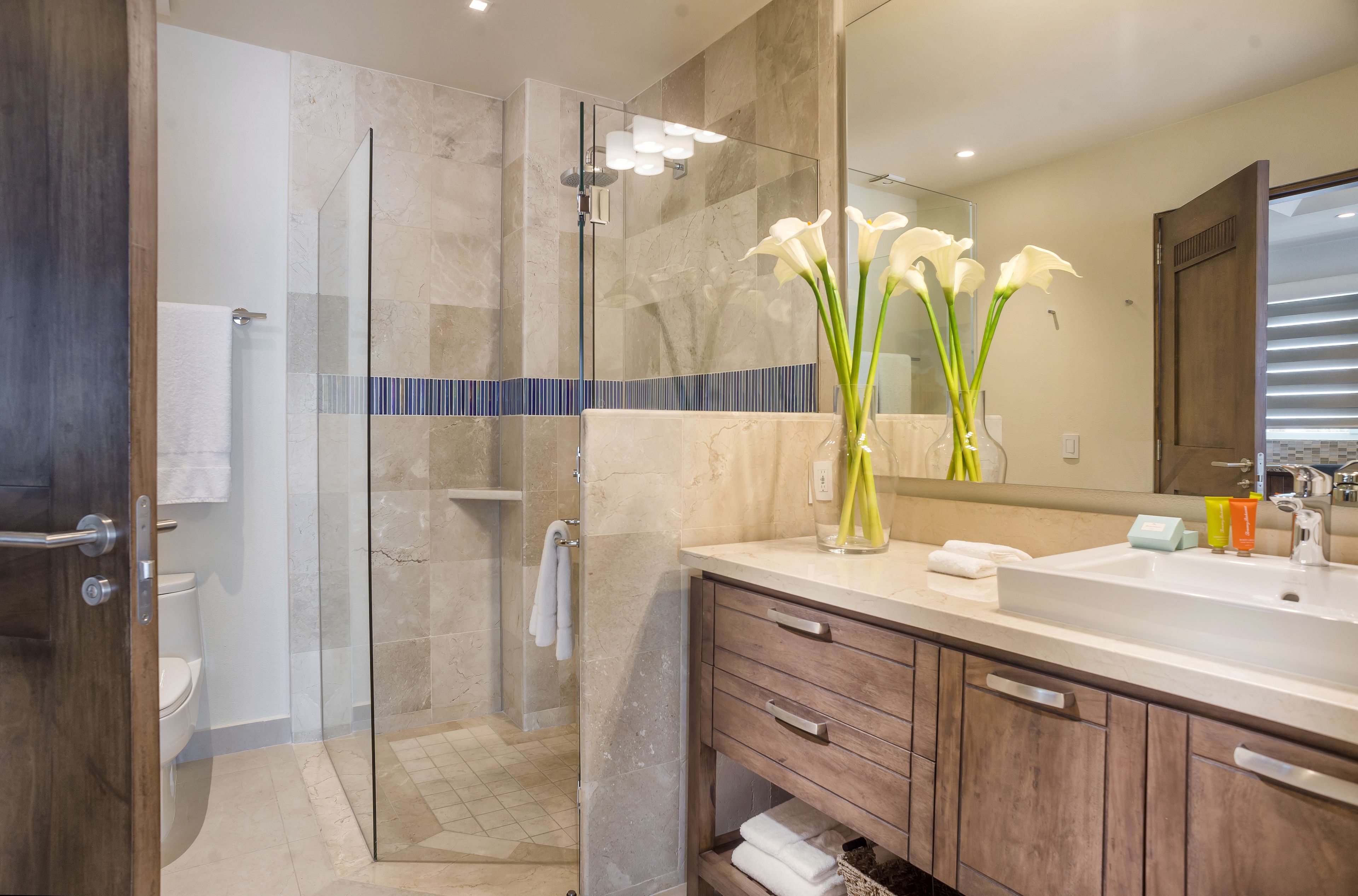 A modern bathroom with a glass-enclosed shower, a large mirror, and a wooden vanity with a sink.
