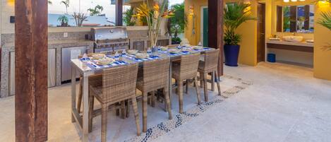 Un'ampia zona pranzo all'aperto con barbecue, sedie in vimini e pavimento piastrellato.